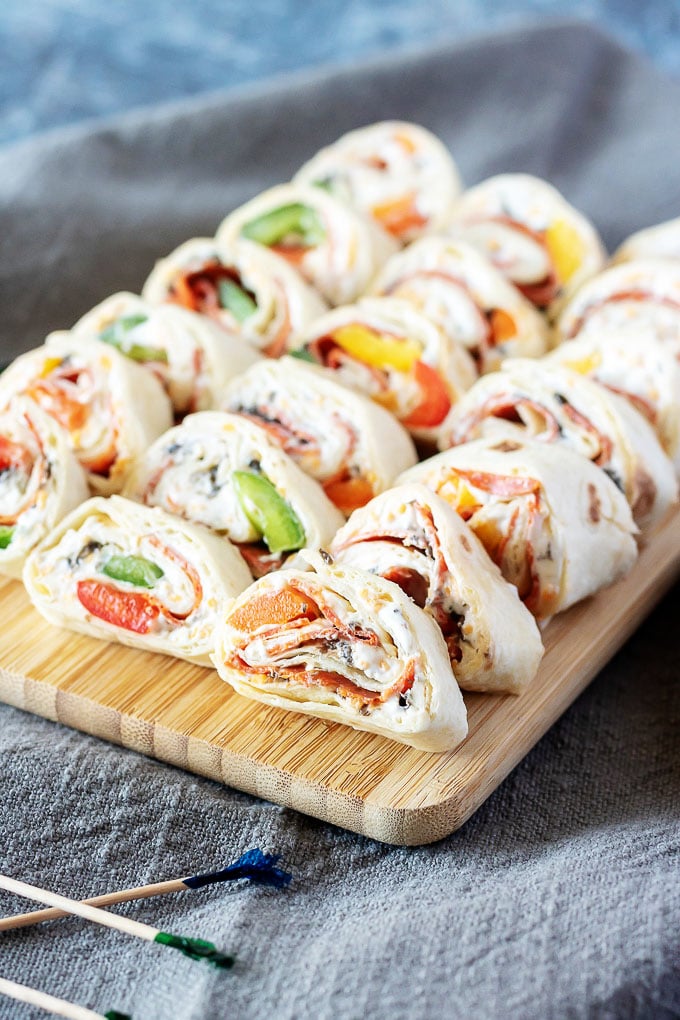 pizza pinwheels laid out in rows on a rectangular wooden cutting board