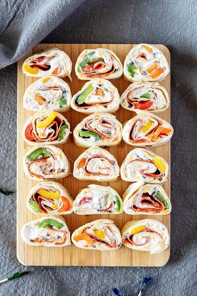 pizza pinwheels laid out in rows on a rectangular wooden cutting board