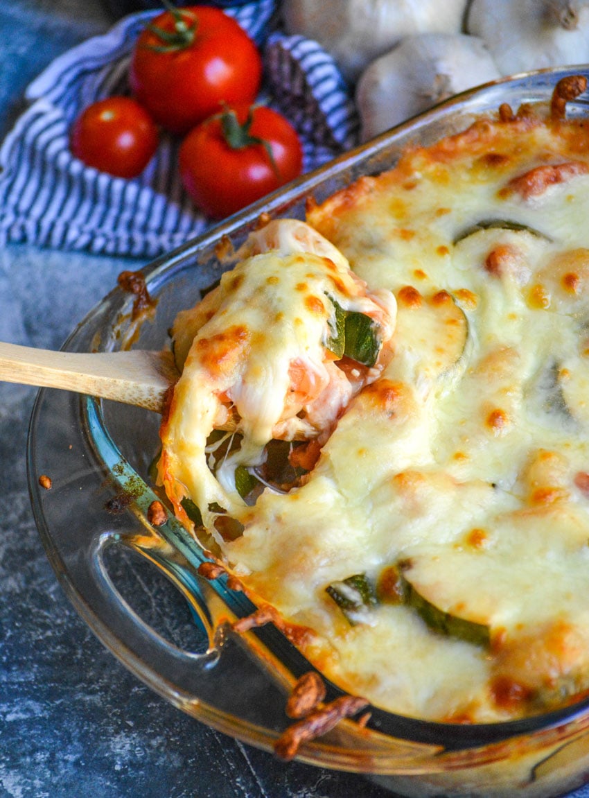 a wooden spoon shown lifting a serving of baked gnocchi with zucchini & tomatoes out of a glass baking dish