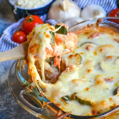 baked gnocchi with zucchini & tomatoes being scooped from a square pyrex baking dish