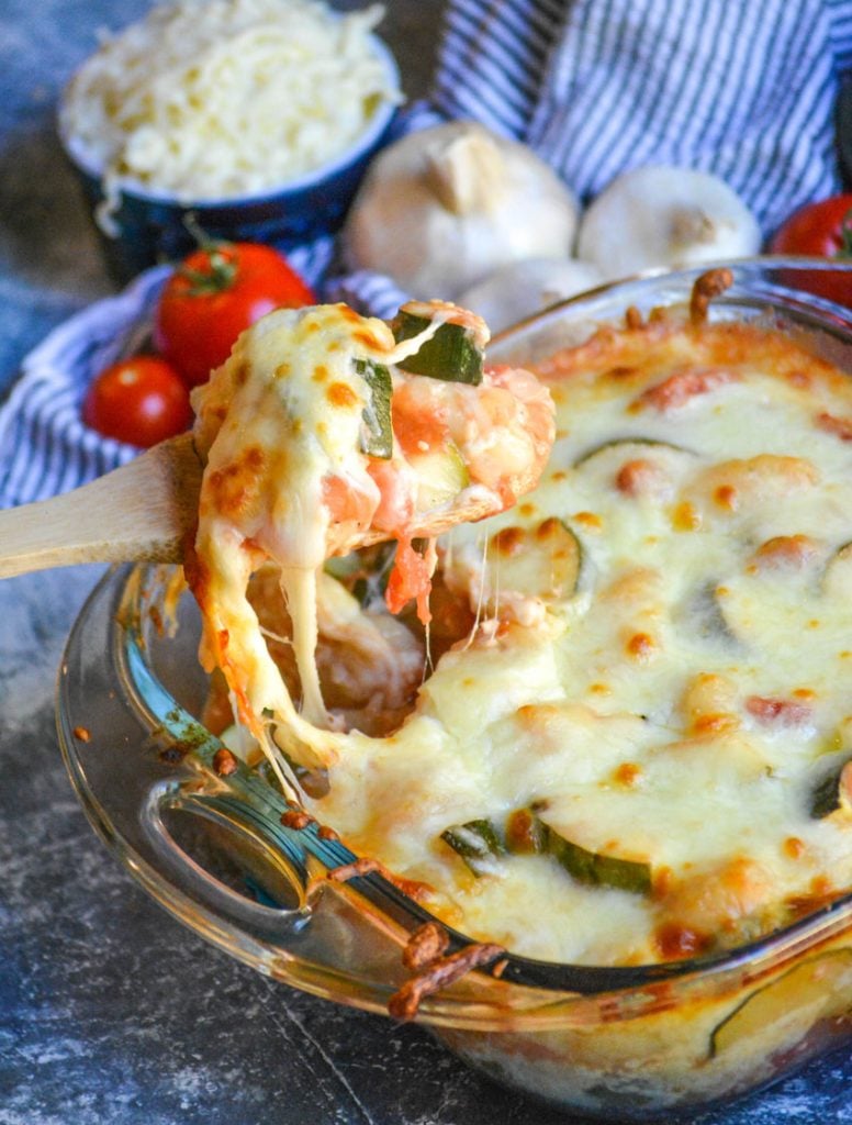 baked gnocchi with zucchini & tomatoes being scooped from a square pyrex baking dish