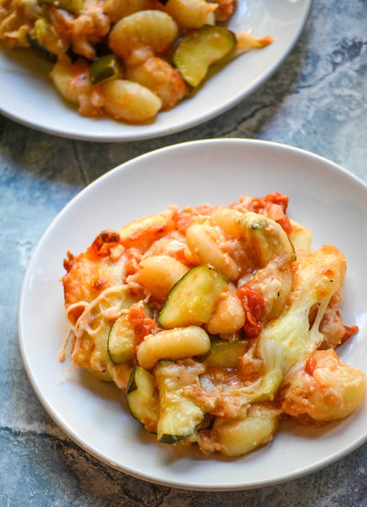 baked gnocchi with zucchini & tomatoes served on white plates
