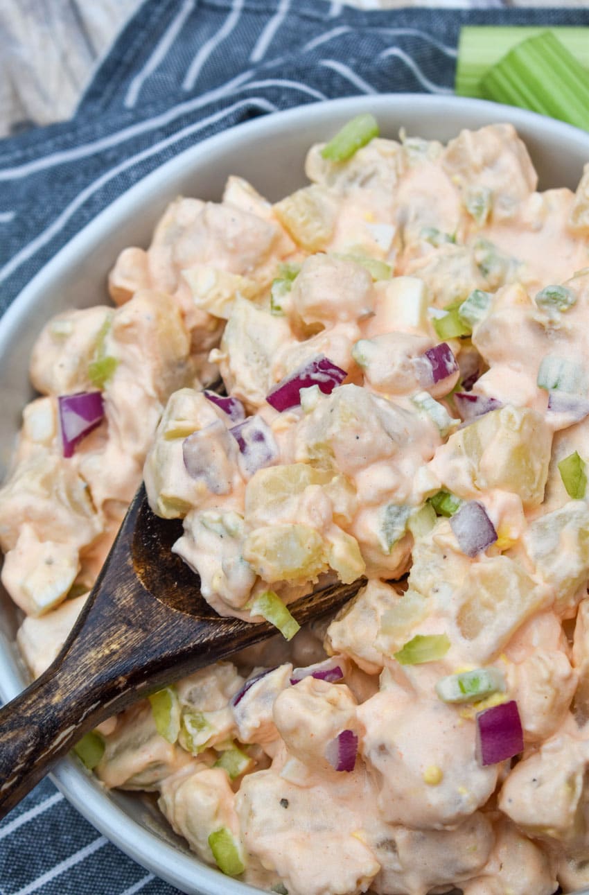 a wooden spoon scooping buffalo potato salad out of a white serving bowl