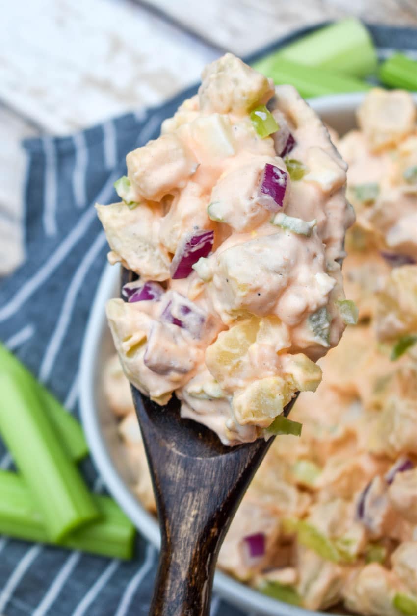 a wooden spoon scooping buffalo potato salad out of a white serving bowl
