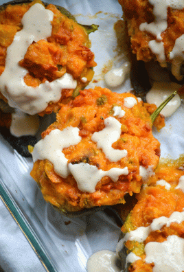 chicken and cornbread stuffed peppers drizzled with ranch sauce in a glass baking dish