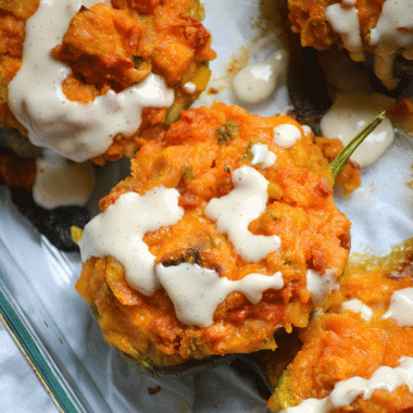 chicken and cornbread stuffed peppers drizzled with ranch sauce in a glass baking dish