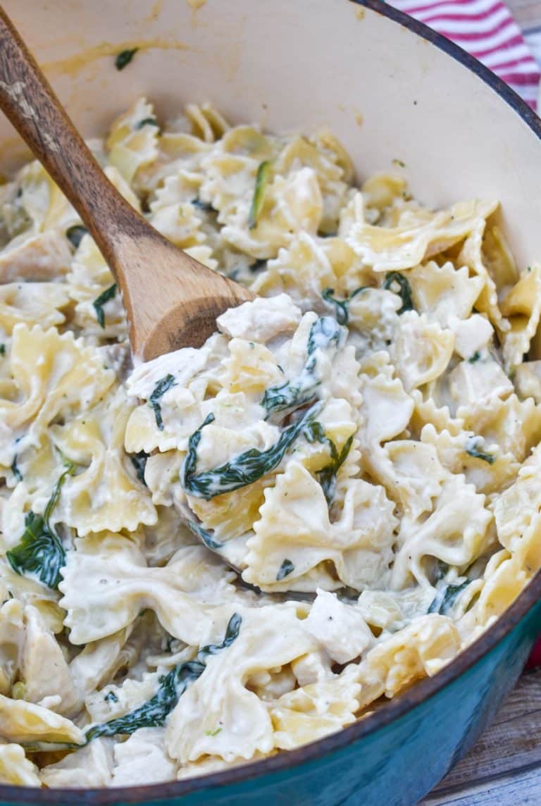 a wooden spoon scooping chicken florentine and farfalle pasta out of a large pot