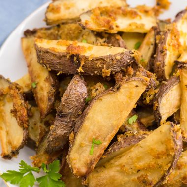 crispy oven baked cheese fries piled high on a white plate with parsley leaves for garnish and a bowl of ketchup in the background