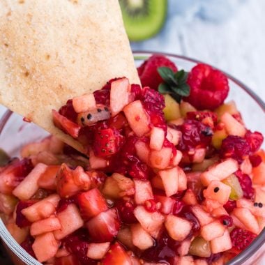 fruit salsa in a clear glass bowl with a cinnamon sugar tortilla chip stuck in it
