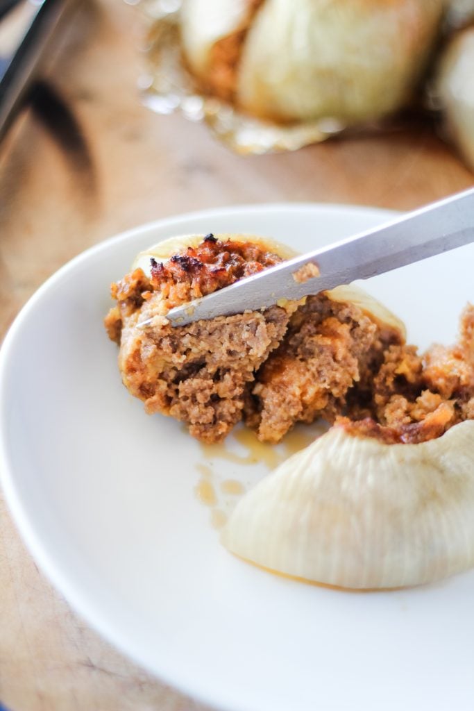 a grilled onion bomb served on a white plate with a knife shown spreading it apart to expose the cooked meat