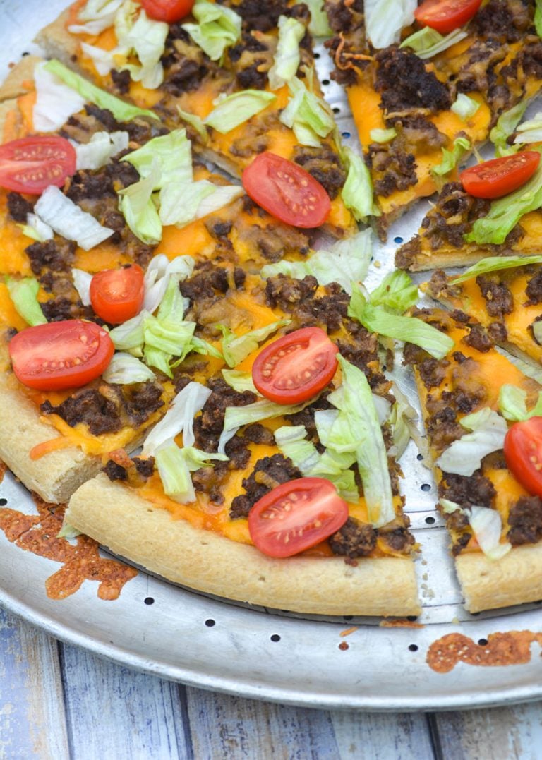 slices of big mac pizza topped with shredded lettuce and sliced tomatoes on a silver pizza pan