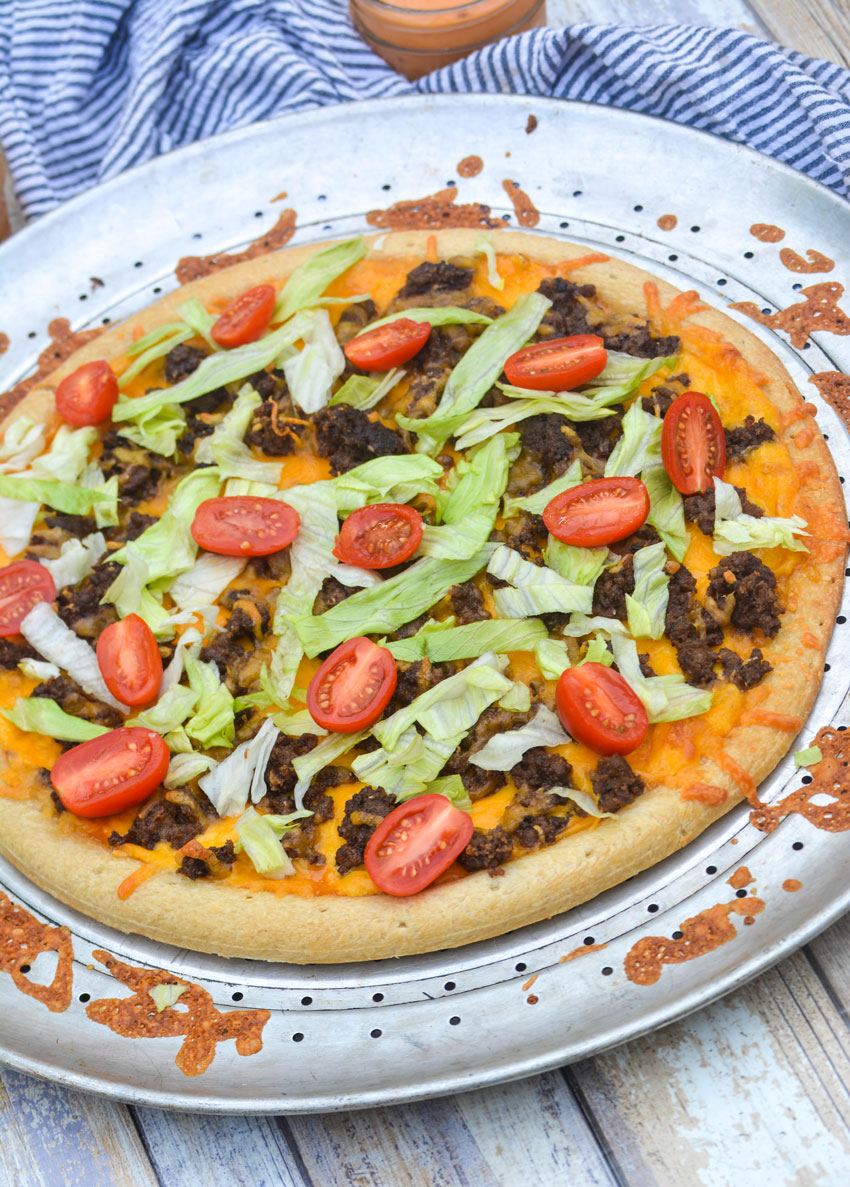 a big mac pizza topped with sliced tomatoes and shredded lettuce on a silver pizza pan