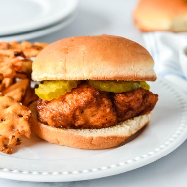 a copycat chick fil sandwich on a white dinner plate with a side of waffles fries