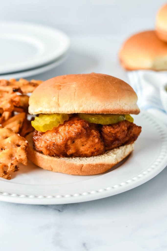 a copycat chick fil sandwich on a white dinner plate with a side of waffles fries