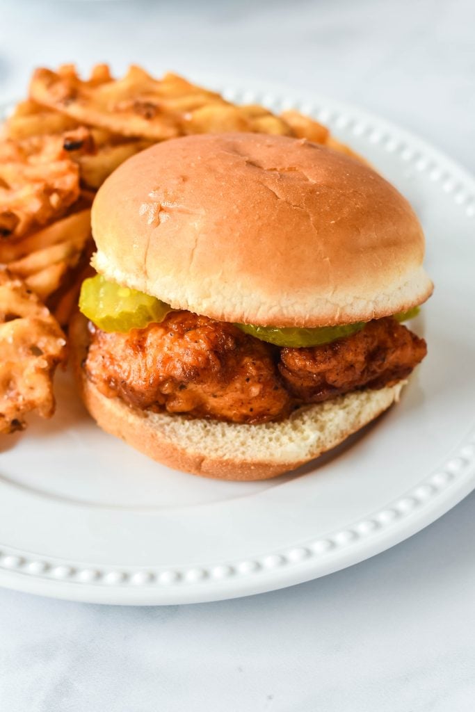 a copycat chick fil sandwich on a white dinner plate with a side of waffles fries