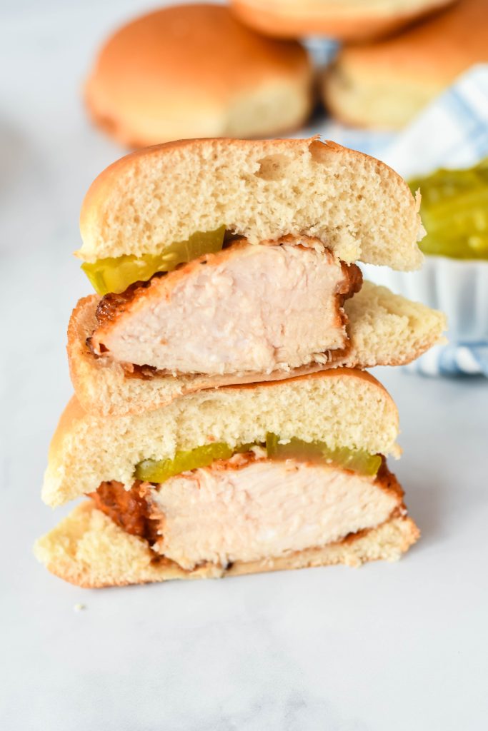 a copycat chick fil a sandwich cut in half, halves stacked on top of each other with fluffy buns and a pickle in the background