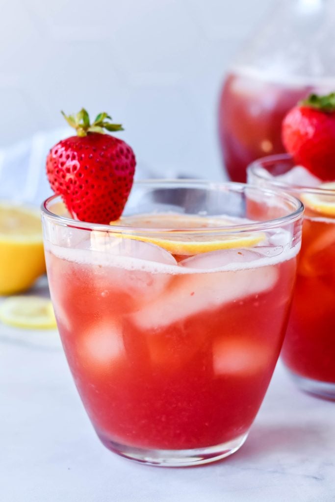 sweet strawberry iced tea served with sliced lemon and fresh strawberry for garnish