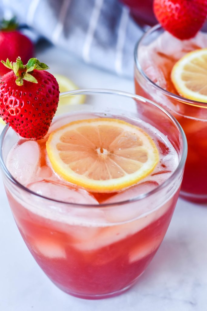 sweet strawberry iced tea served with sliced lemon and fresh strawberry for garnish