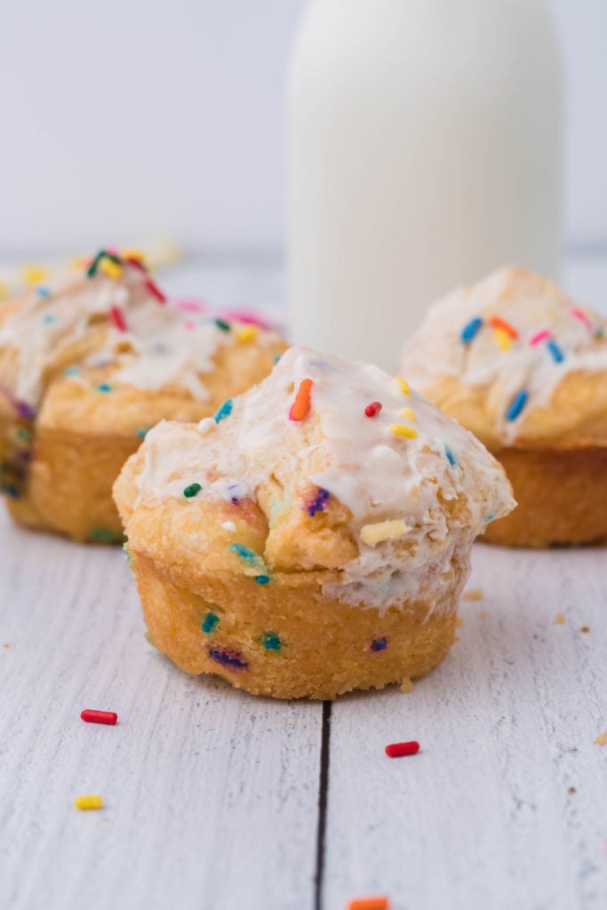 three cake batter monkey muffins shown on a wooden table in front of a glass of milk