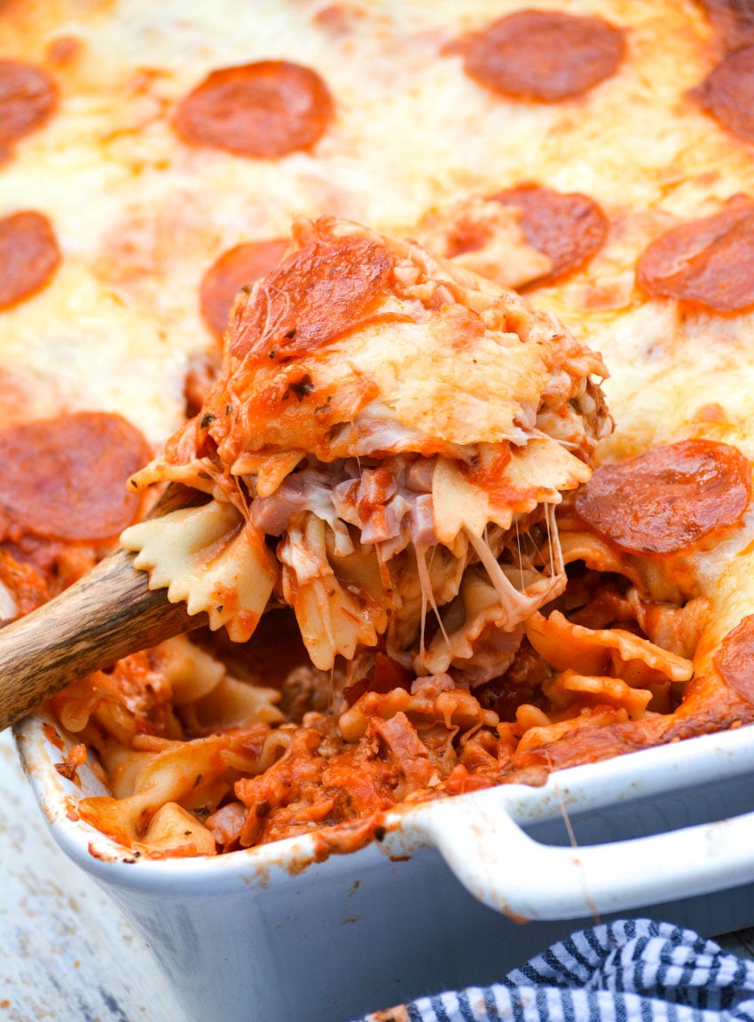 a wooden spoon digging into a meat lovers pizza casserole in a white dish