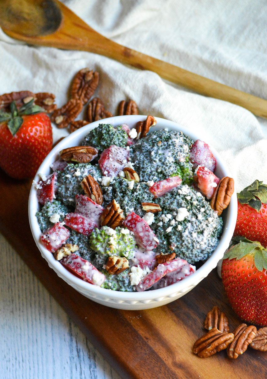 creamy strawberry broccoli salad studded with pecans and served in a white bowl on a wooden cutting board