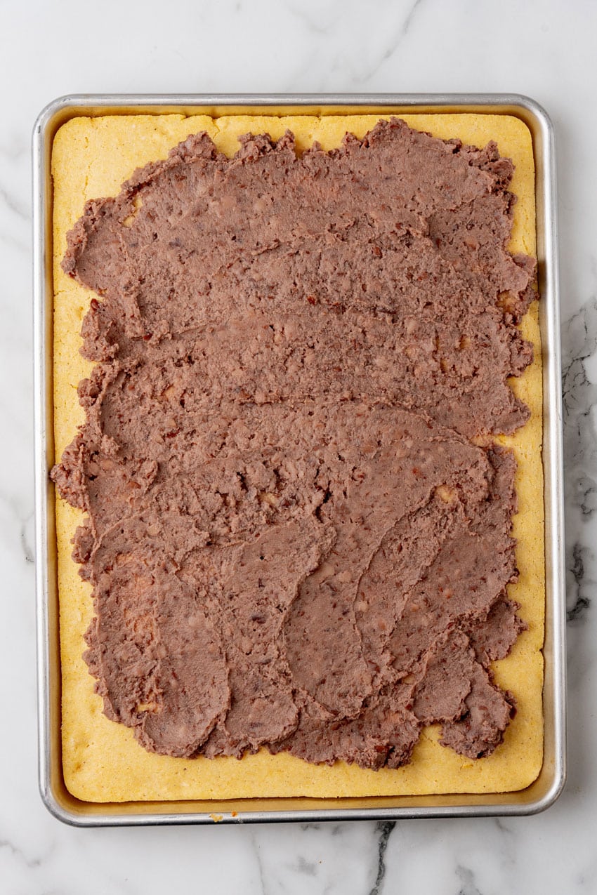 refried beans spread out in an even layer over baked sheet pan cornbread