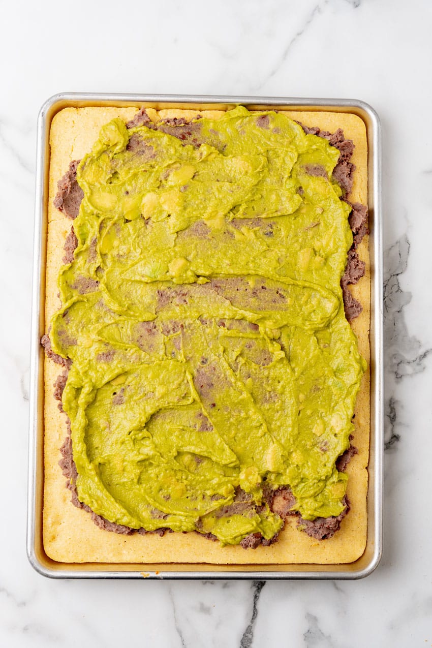 guacamole spread out in an even layer over baked sheet pan cornbread