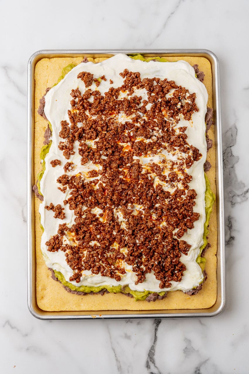 7 layers of dip spread over baked cornbread on a metal sheet pan
