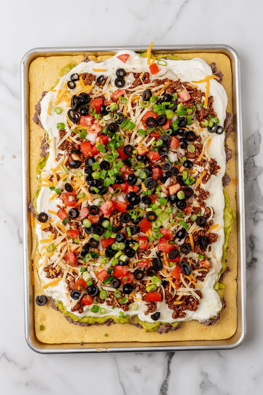 7 layers of dip spread over baked cornbread on a metal sheet pan