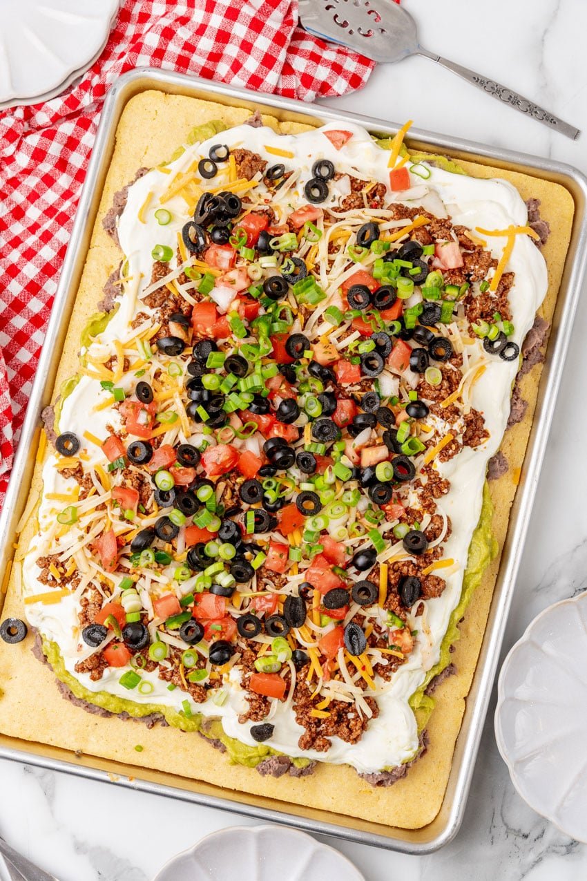7 layers of dip spread over baked cornbread on a metal sheet pan