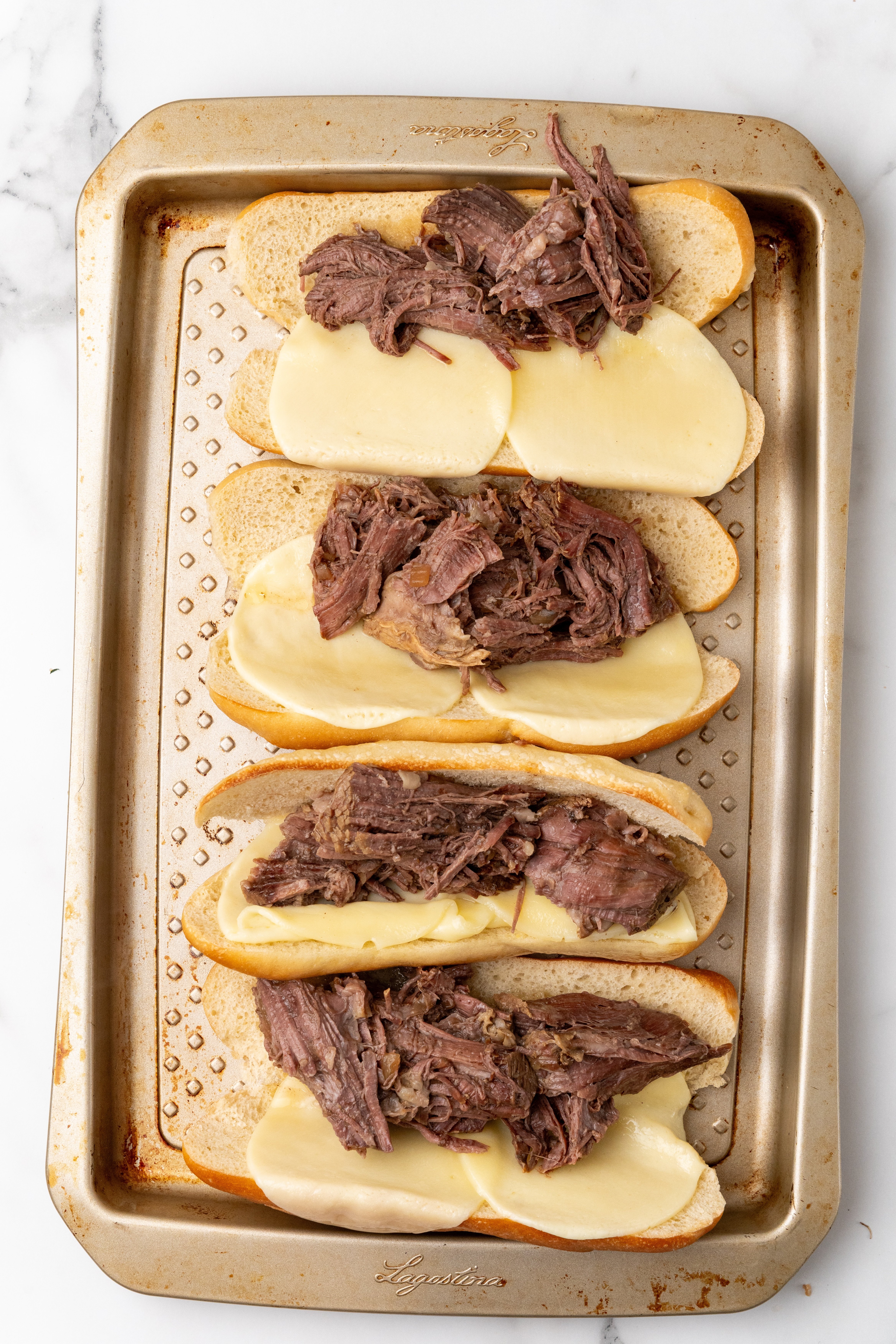 french dip beef on top of melted provolone cheese on toasted buns on a metal sheet pan