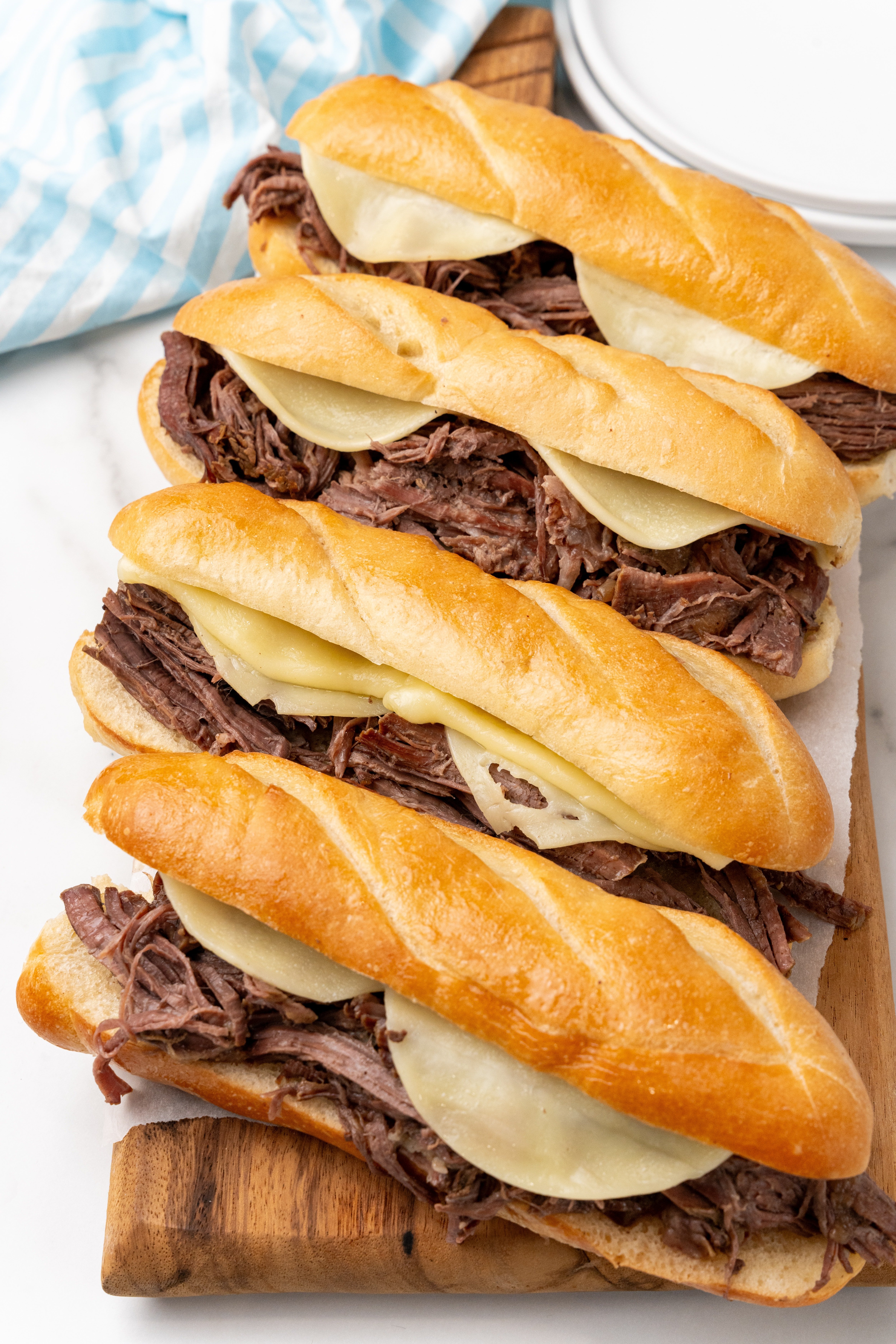 a row of crockpot french dip sandwiches on a wooden cutting board