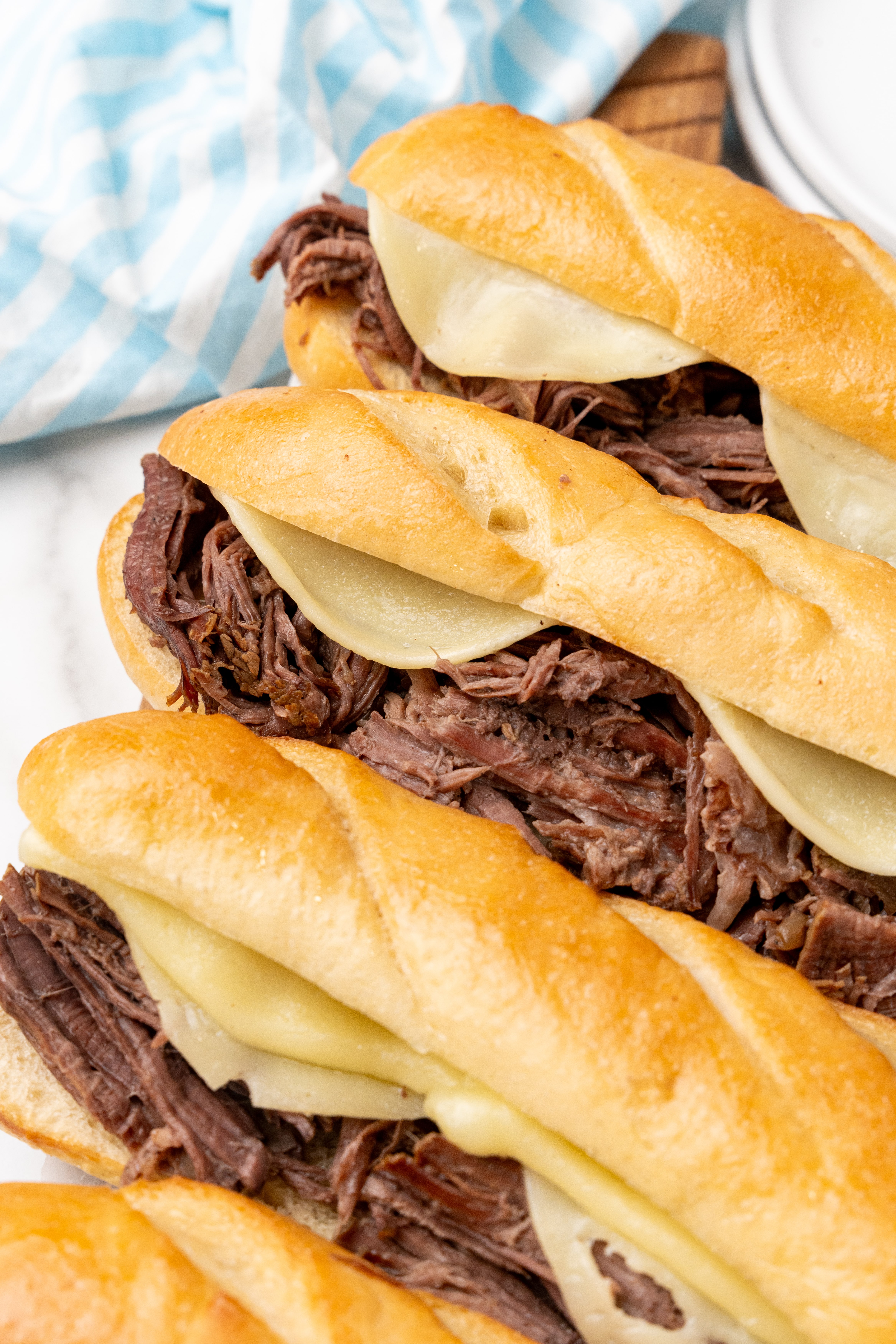 a row of crockpot french dip sandwiches on a wooden cutting board