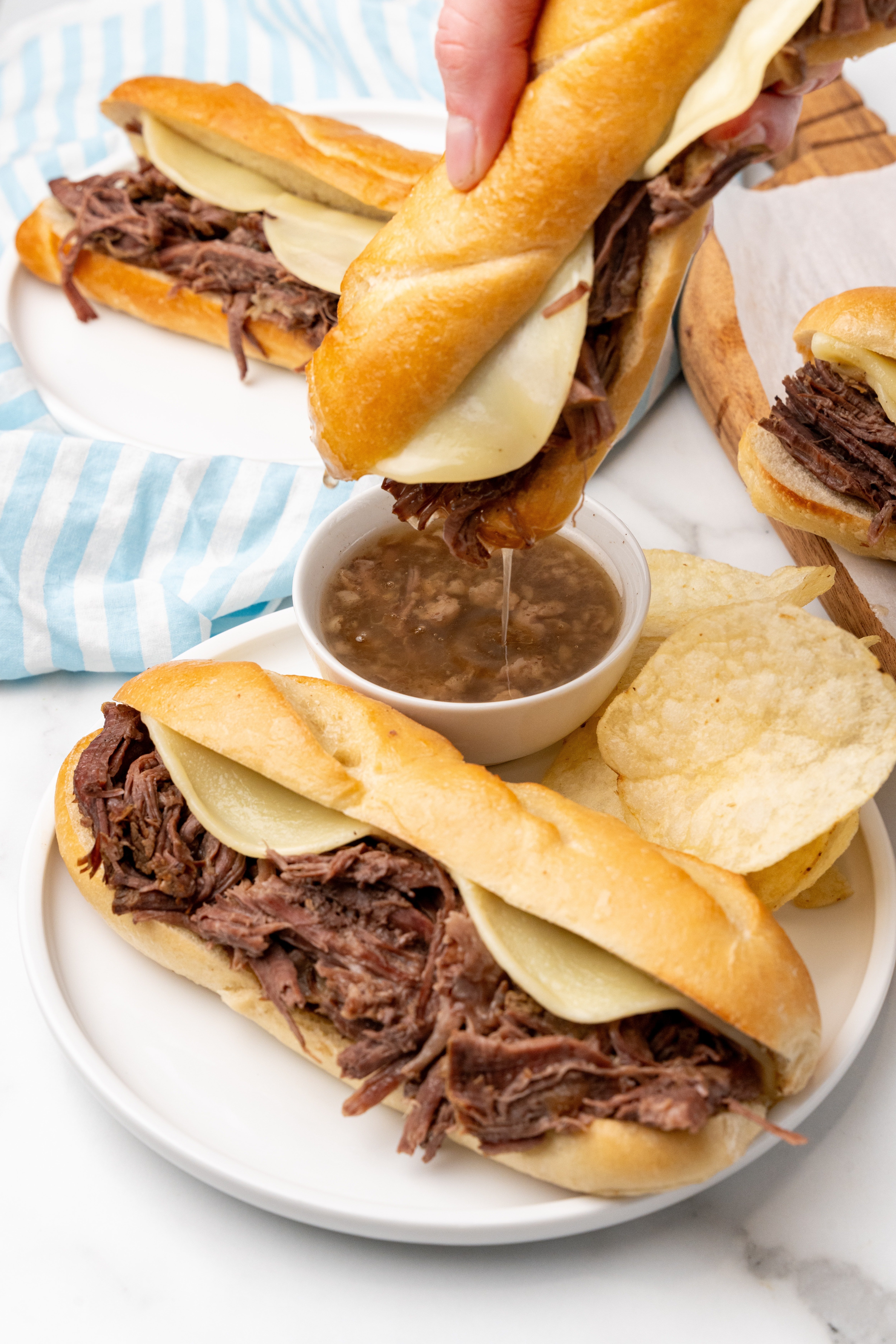 a crockpot french dip sandwich being dunked in a small white bowl filled with au jus