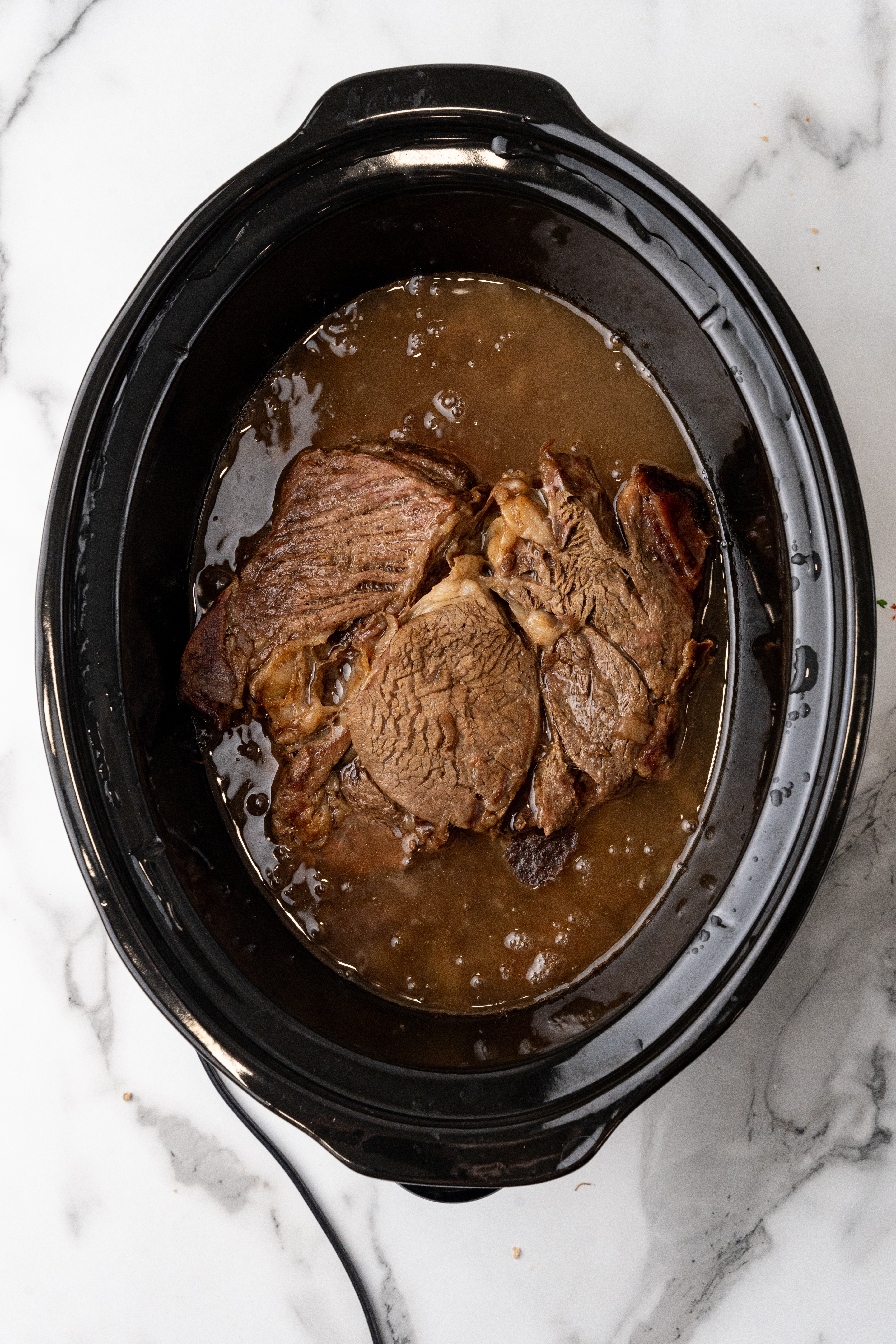 slow cooked chuck roast beef in juices in the black bowl of a crockpot