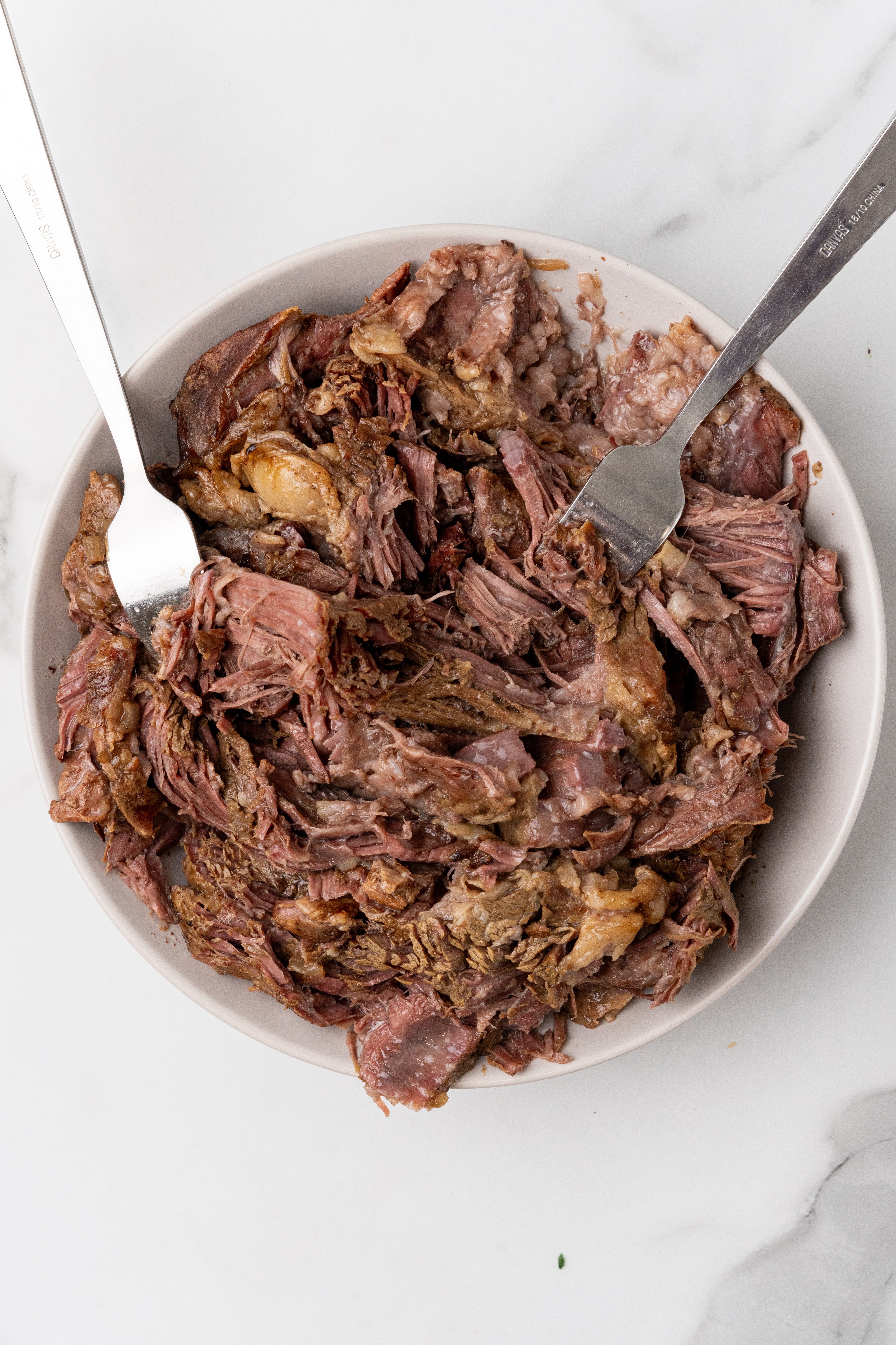 shredded roast beef in a white bowl with two forks resting on the side