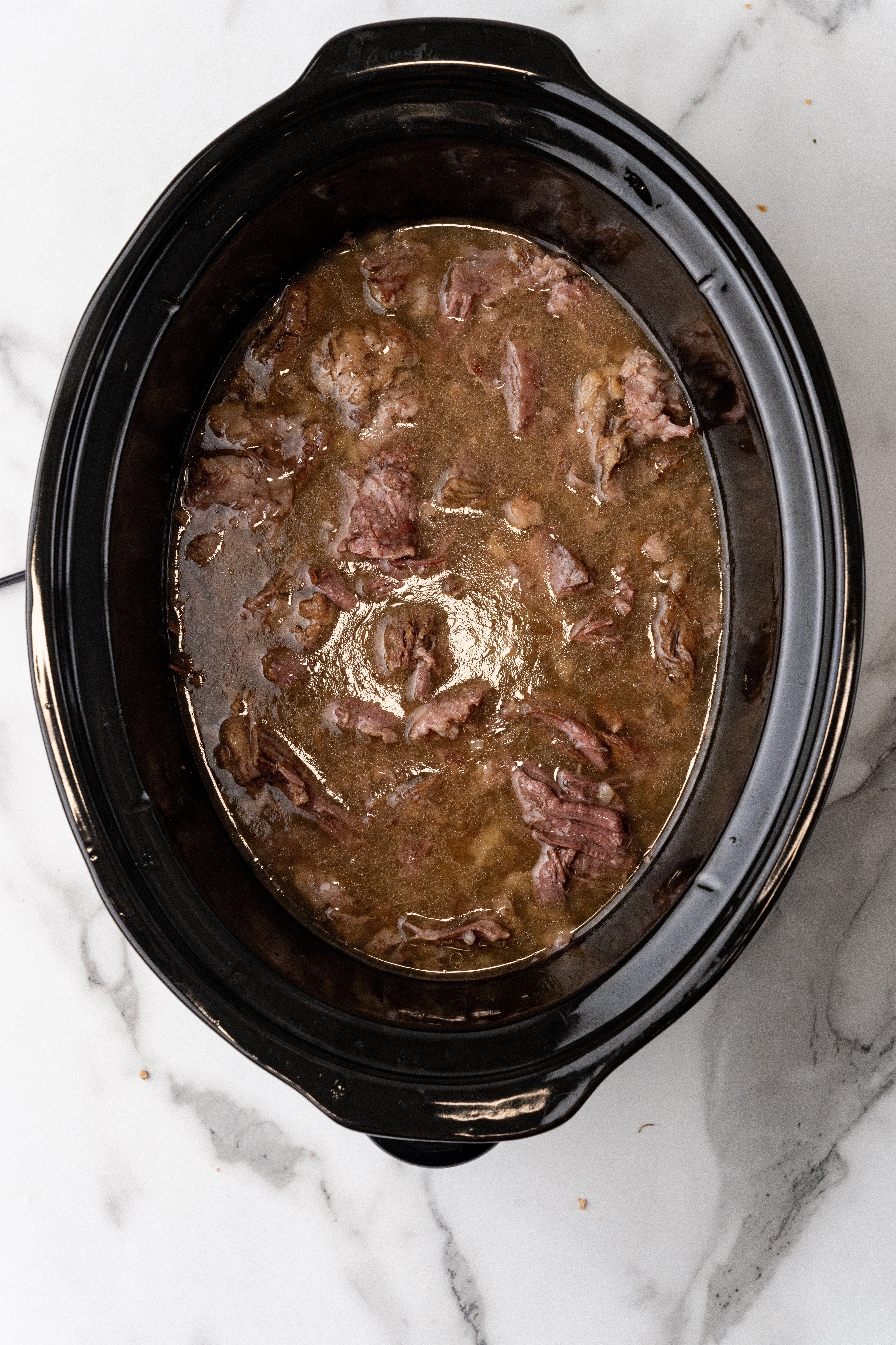 slow cooker french dip beef in the bowl of a black crockpot