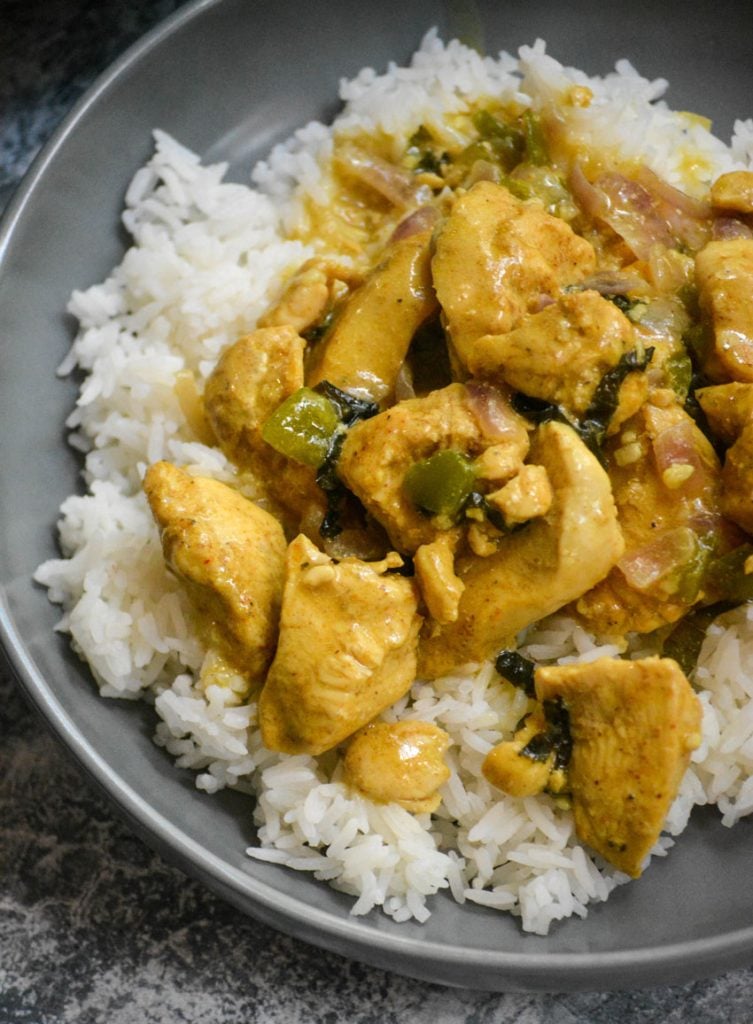 Basil Chicken in Coconut Curry Sauce spread over a bed of steamed white rice in a gray bowl