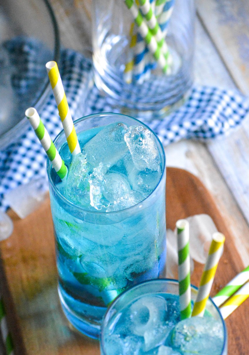copycat sonic ocean water in two tall glasses with paper straws on a narrow wooden cutting board