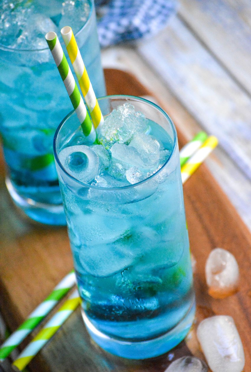 copycat sonic ocean water in two tall glasses with paper straws on a narrow wooden cutting board