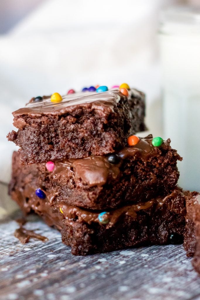 a stack of fudgey cosmic chocolate brownies on a weathered wooden back drop with a glass of cold milk in the background