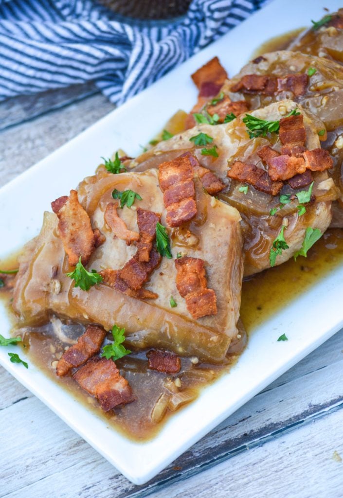 crockpot smothered pork chops shown served on a white platter with a sprinkle of fresh green herbs