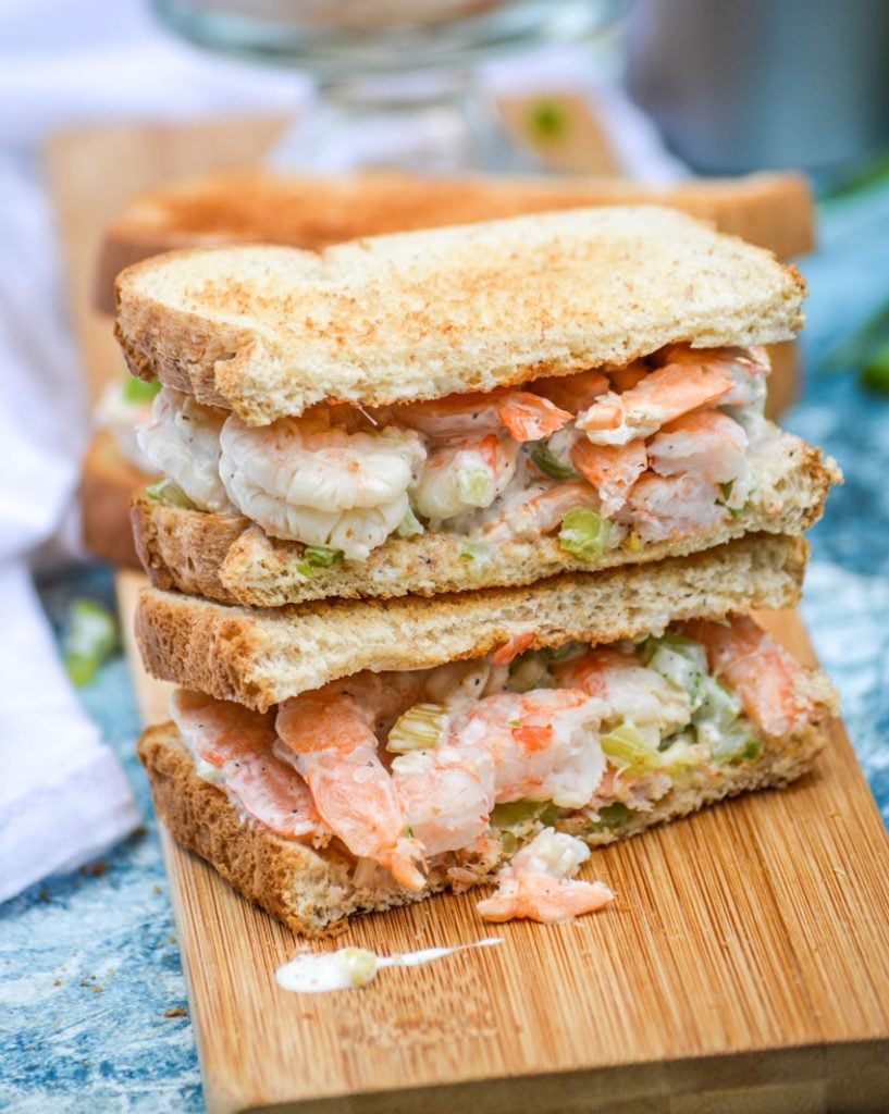 a creamy shrimp salad on toasted bread, the sandwich is cut in half to show the filling