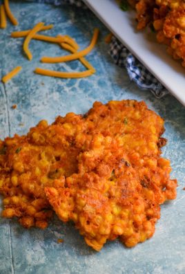 sweet corn and cheddar cheese fritters sitting in a pile on a blue backdrop