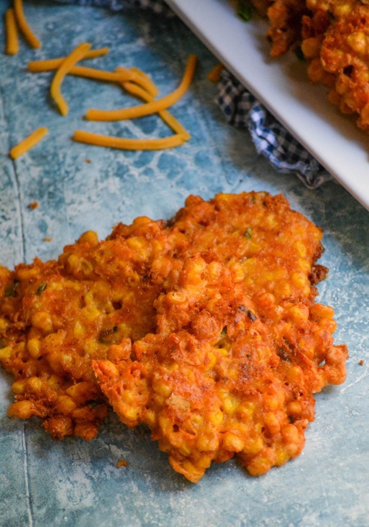 sweet corn and cheddar cheese fritters sitting in a pile on a blue backdrop