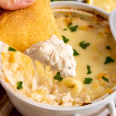 a hand holding a baked wonton chip topped with crab rangoon dip