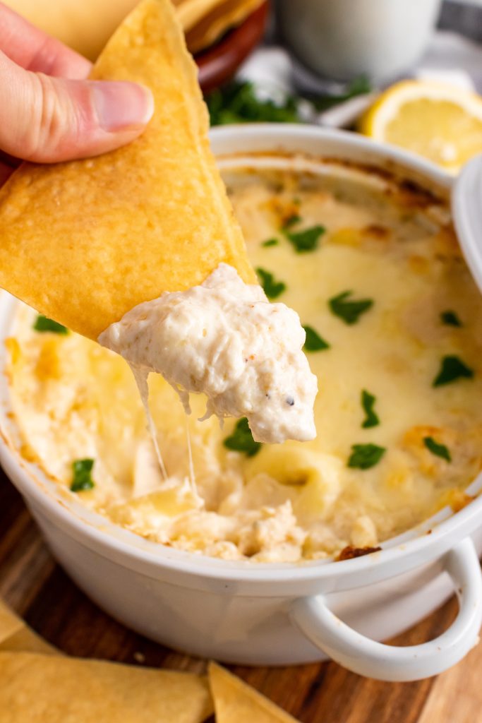 a hand holding a baked wonton chip topped with crab rangoon dip