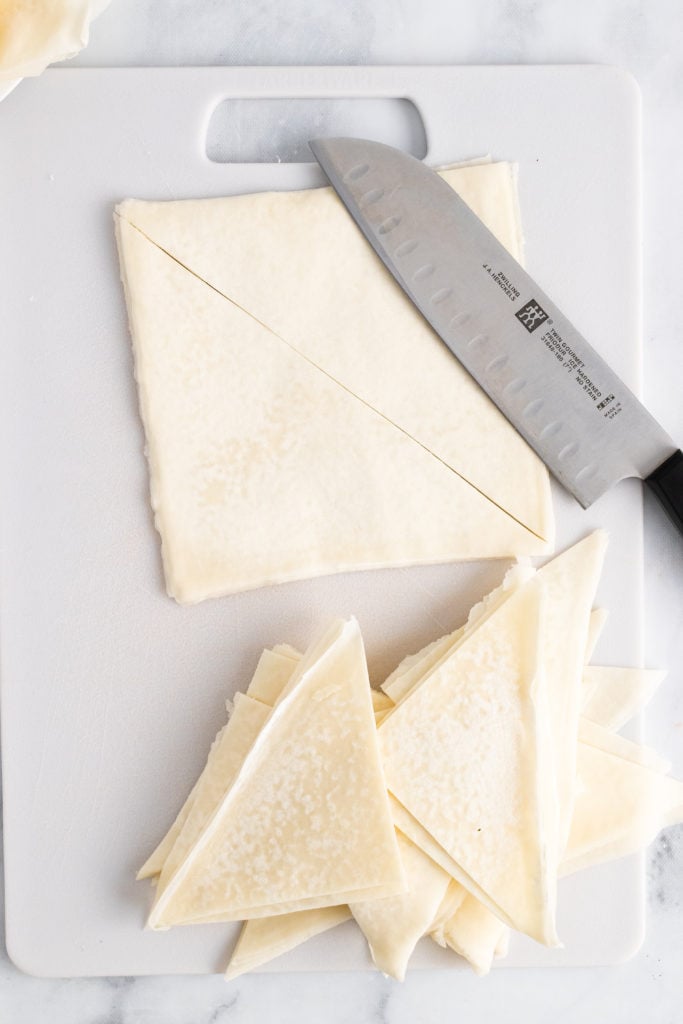 a knife shown with cut wonton wrappers on a white cutting board