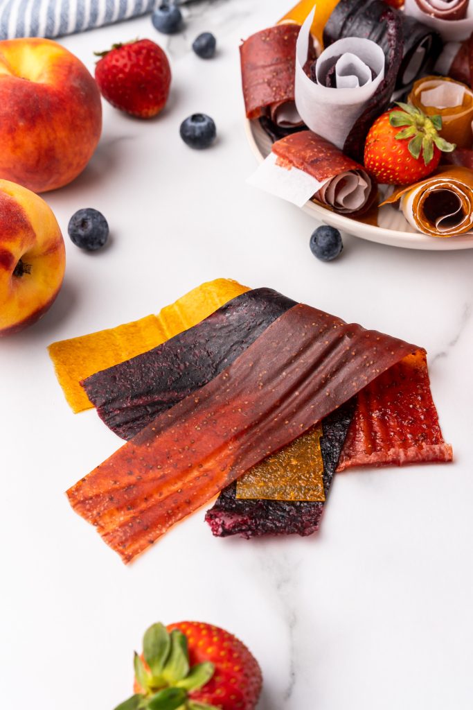 strips of 3 ingredient fruit leather next to fresh fruits on a clean countertop