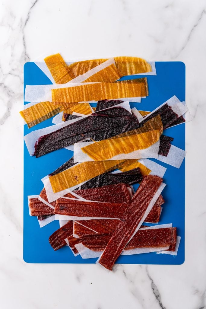 strips of parchment paper lined fruit leather laying out on a silicone cutting mat